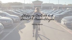 someone cycling between parked cars outside a shopping centre while interpreting Bangor from a bicycle